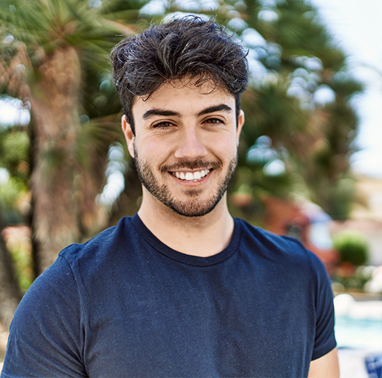 Young man with a bright, confident smile outdoors, representing patients served by Dr. Rachel Ryu at Hillcrest Glow Dental Office in the greater San Diego community 